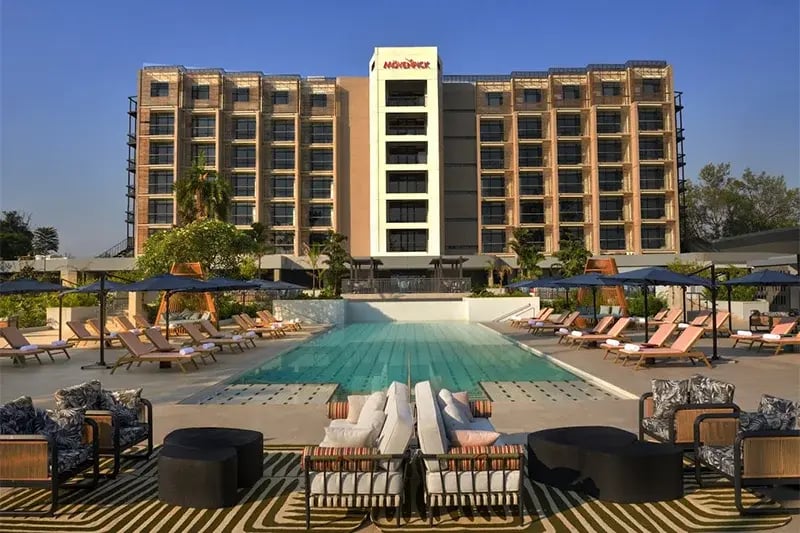 Modern hotel exterior with a central pool surrounded by sun loungers and shaded seating. The setting conveys a luxurious, relaxing atmosphere.