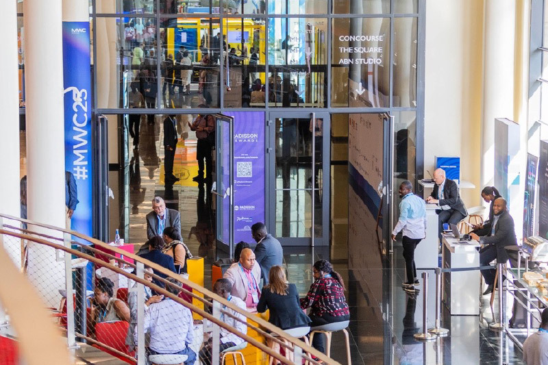 Crowds and seated attendees at the entrance area of MWC, with signage for #MWC23 and “Concourse The Square ABN Studio” visible through glass doors.