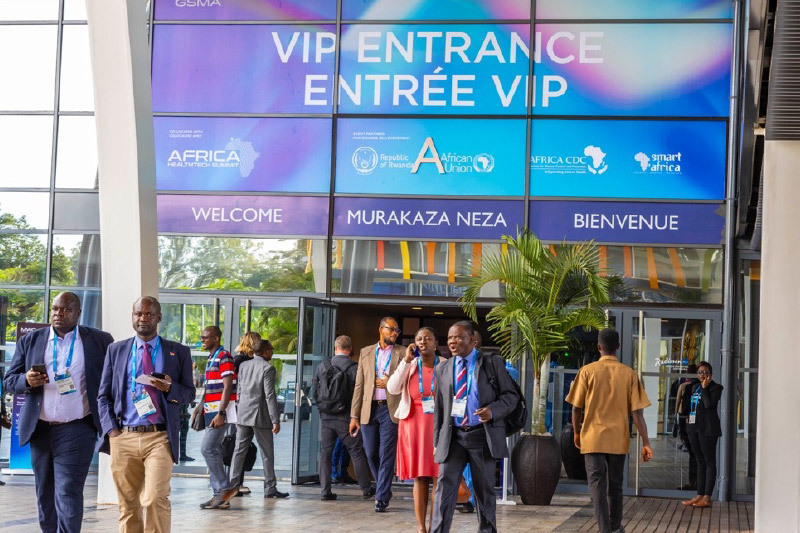 Attendees exit the VIP entrance of a convention centre during the Africa HealthTech Summit, with welcome signs in multiple languages and banners for the Republic of Rwanda, African Union, Africa CDC, and Smart Africa displayed above.