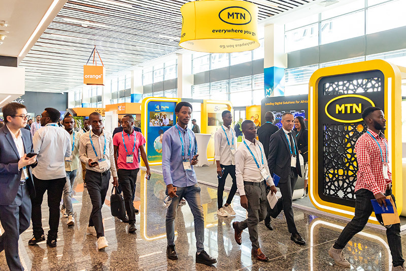 Attendees walk through a brightly lit exhibition area featuring MTN and Orange booths at MWC, with large branded signage and displays promoting digital solutions for Africa.